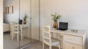 Quarto com cama, escrivaninha com laptop, cadeira, guarda-roupa e espelho.