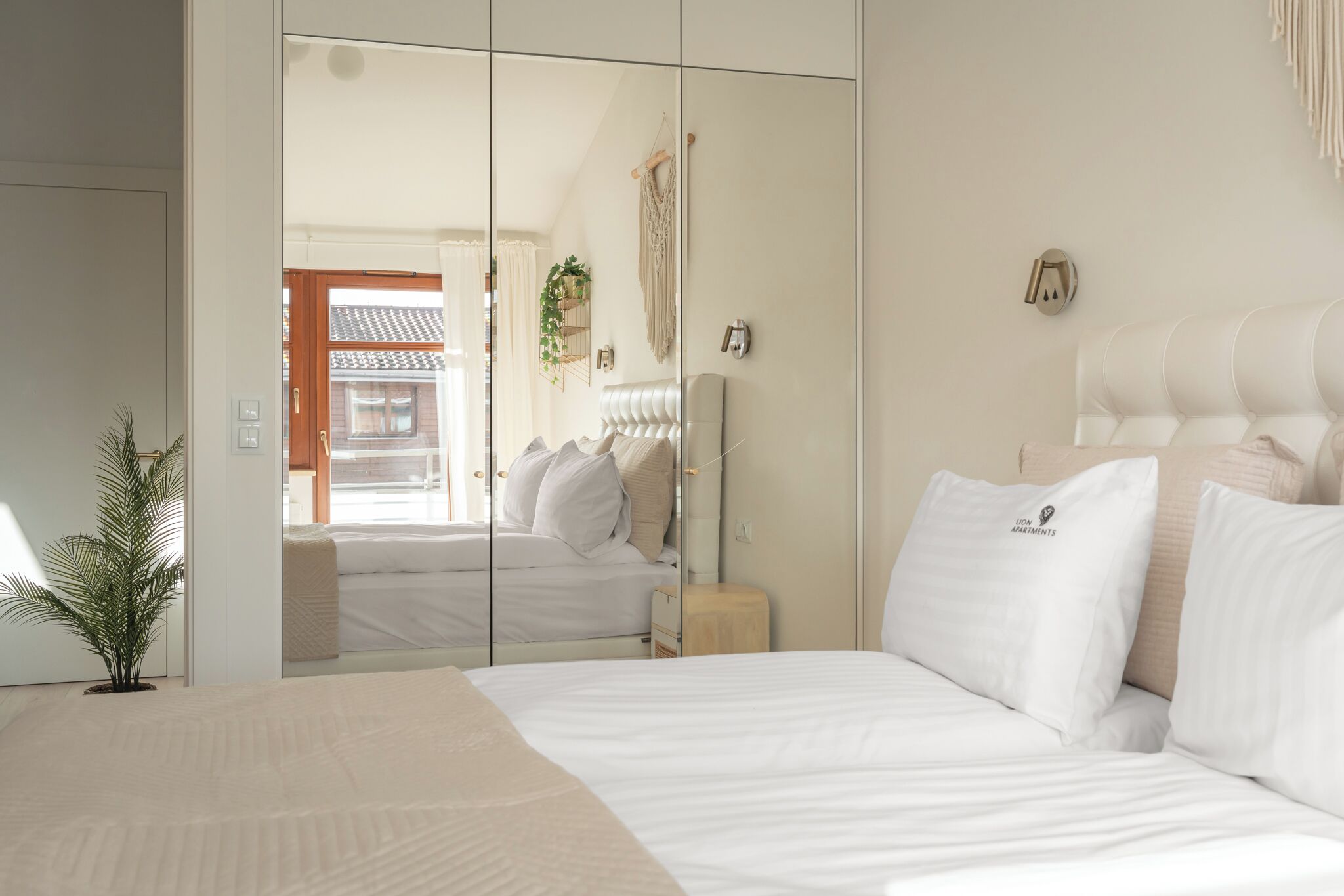 A bedroom with a bed, a mirror, a bedside table, and a potted plant.