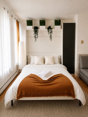 A modern bedroom with a large bed, a bedside table, a lamp, a sofa, and a door. - Mondo Downtown Montreal Studio | Steps from Old Port (Montréal)