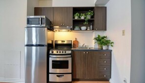 A compact kitchen with a built-in microwave, oven, and stovetop. - Mondo Downtown Montreal Studio | Steps from Old Port (Montréal)
