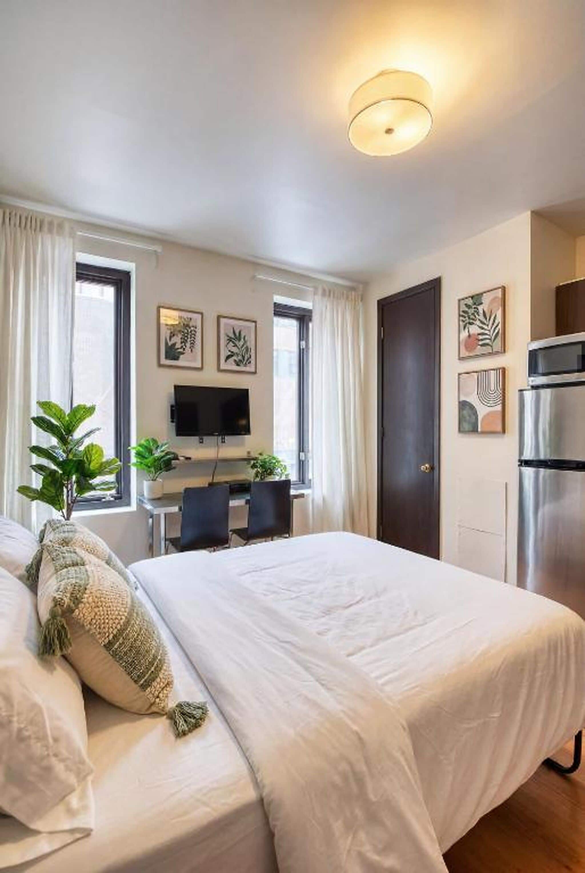 A hotel room with a bed, a desk with a flat-screen TV, a door, and a kitchenette.