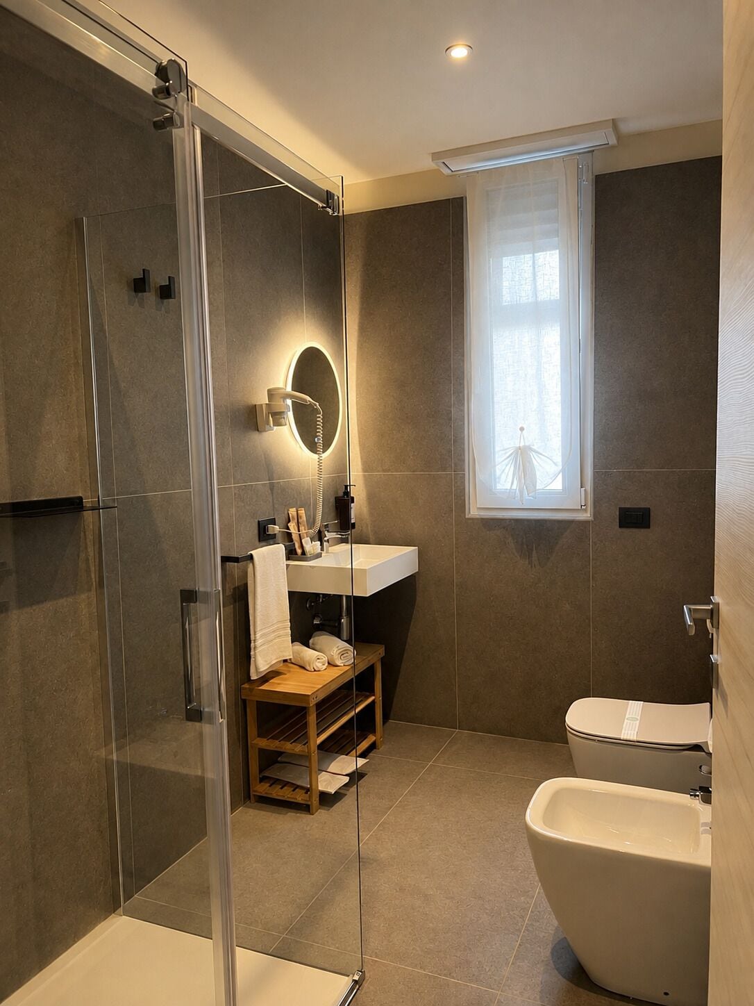 A modern bathroom with a glass shower enclosure, a standalone bathtub, and a window providing natural light.