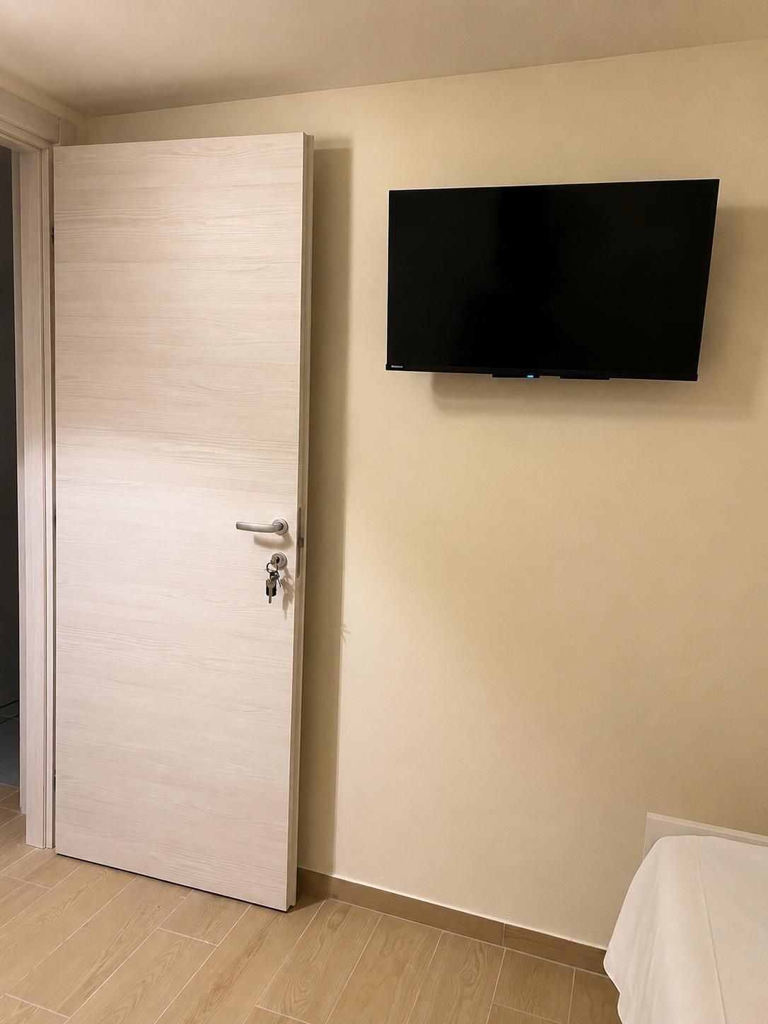 Una stanza con la porta chiusa, una televisione a muro e un asciugamano bianco su una superficie.