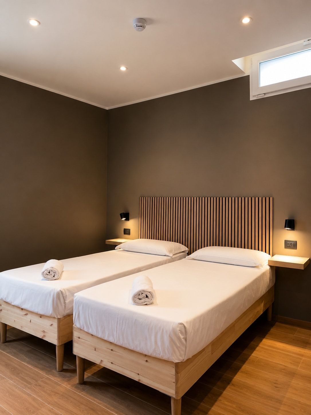 Une chambre d’hôtel avec deux lits simples, des têtes de lit en bois, des tables de chevet avec des lampes et un luminaire au plafond.