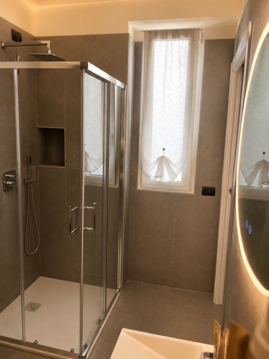 Un bagno moderno con box doccia in vetro, una vasca da bagno bianca e una finestra con tende trasparenti.