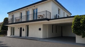Een modern gebouw met twee verdiepingen, een balkon, een plat dak en een kleine tuin.