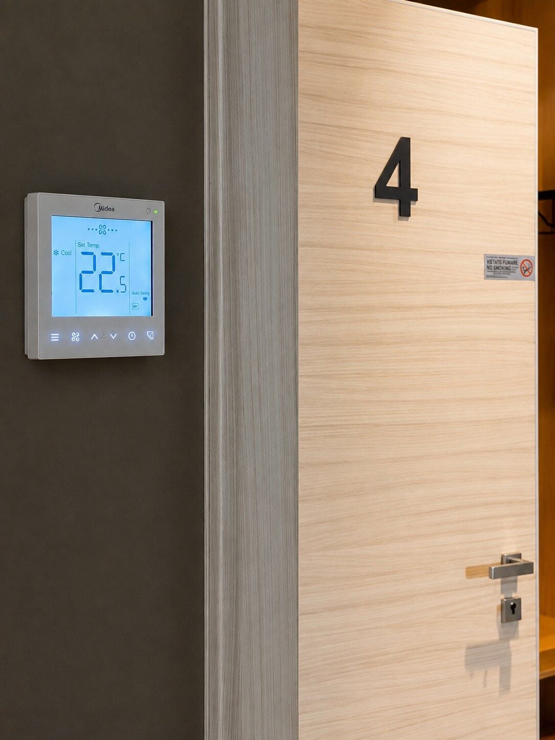 A digital thermostat displaying a temperature of 22.5°C, a wooden door with the number 4, and a no-smoking sign.