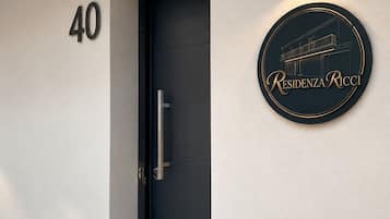 Vestíbulo moderno de un edificio con una puerta oscura, un cartel con el número '40' y un letrero circular que dice 'Residenza Ricci'.