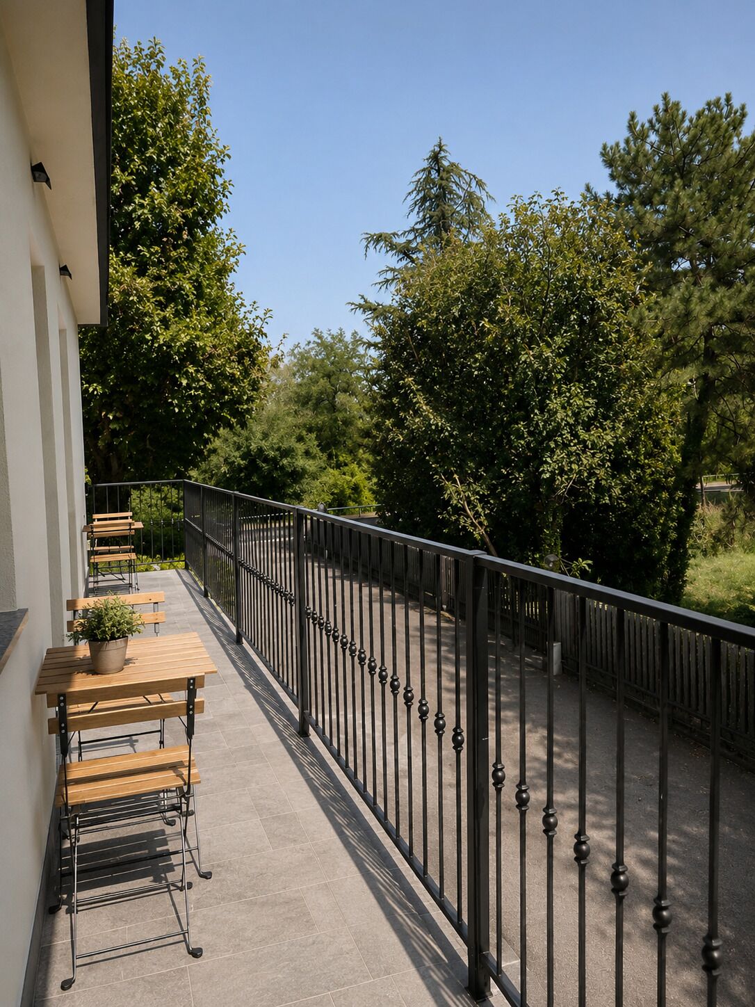 Ein Balkon mit Metallgeländer, Holzbanken und einem Blumentopf.