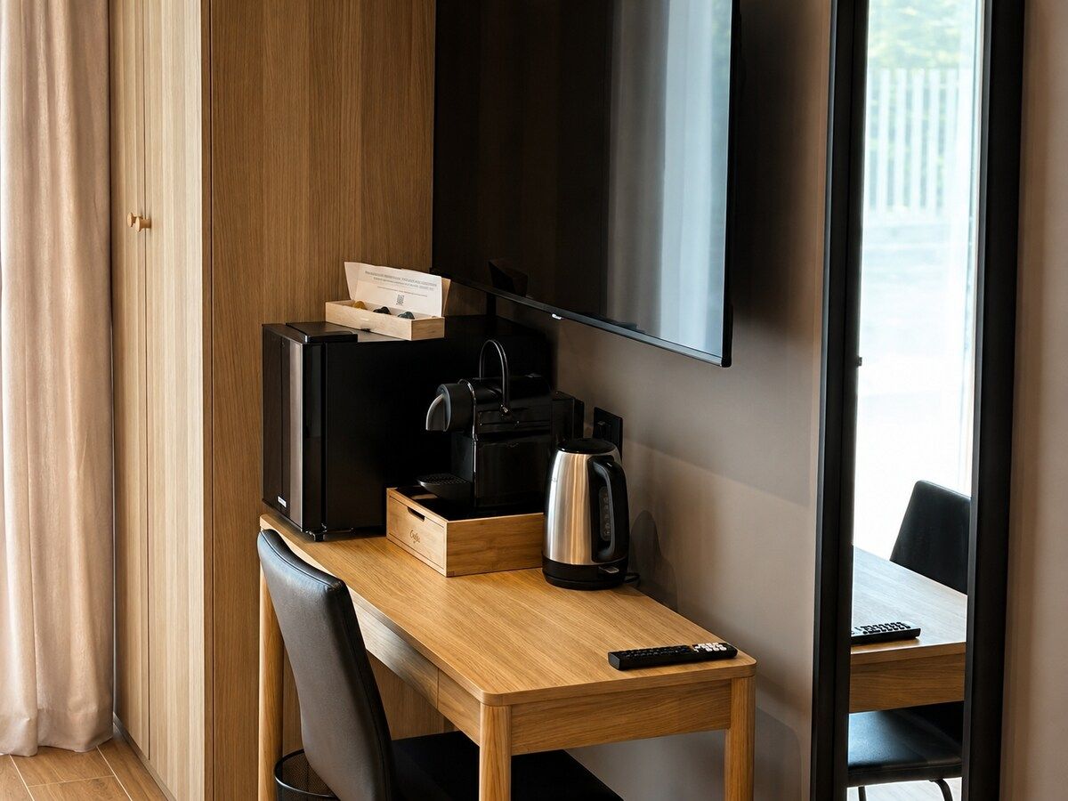 Habitación de hotel con escritorio de madera, televisor, cafetera y control remoto.