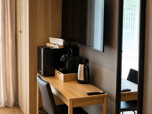 Habitación de hotel con escritorio de madera, televisor, cafetera y control remoto.