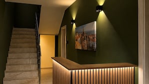 Een receptiegedeelte met een houten receptiebalie, een trap en een aan de muur bevestigd schilderij.