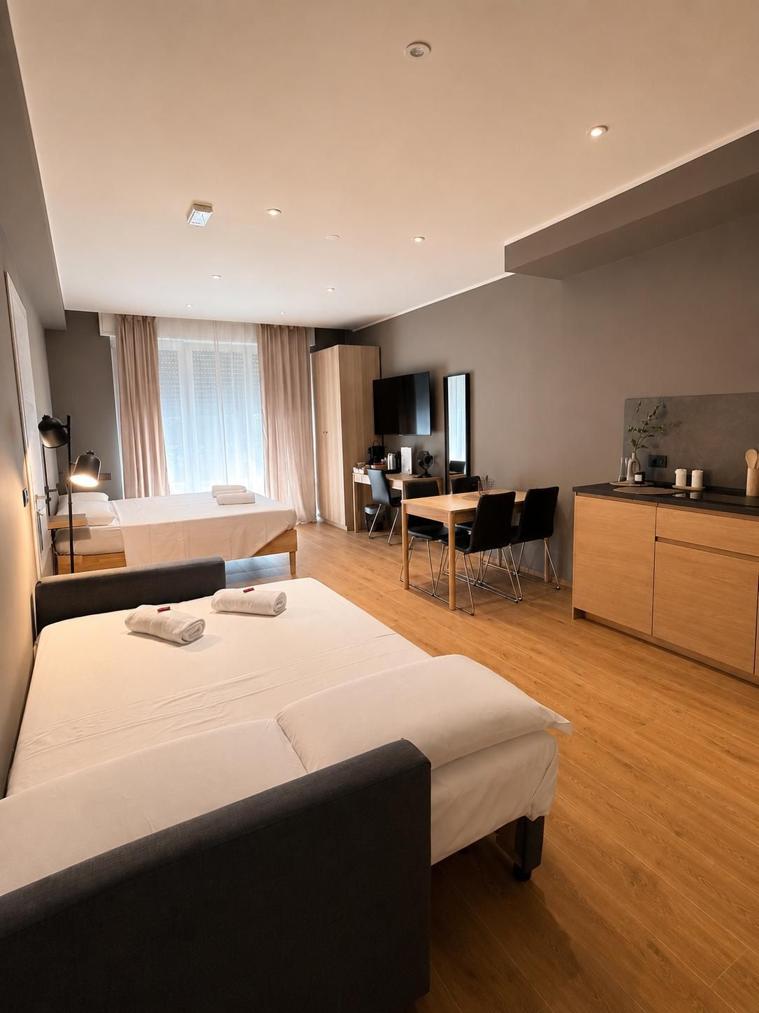Ein modernes Hotelzimmer mit Bett, Schreibtisch, Stuhl, Fernseher und einer Küchenzeile.