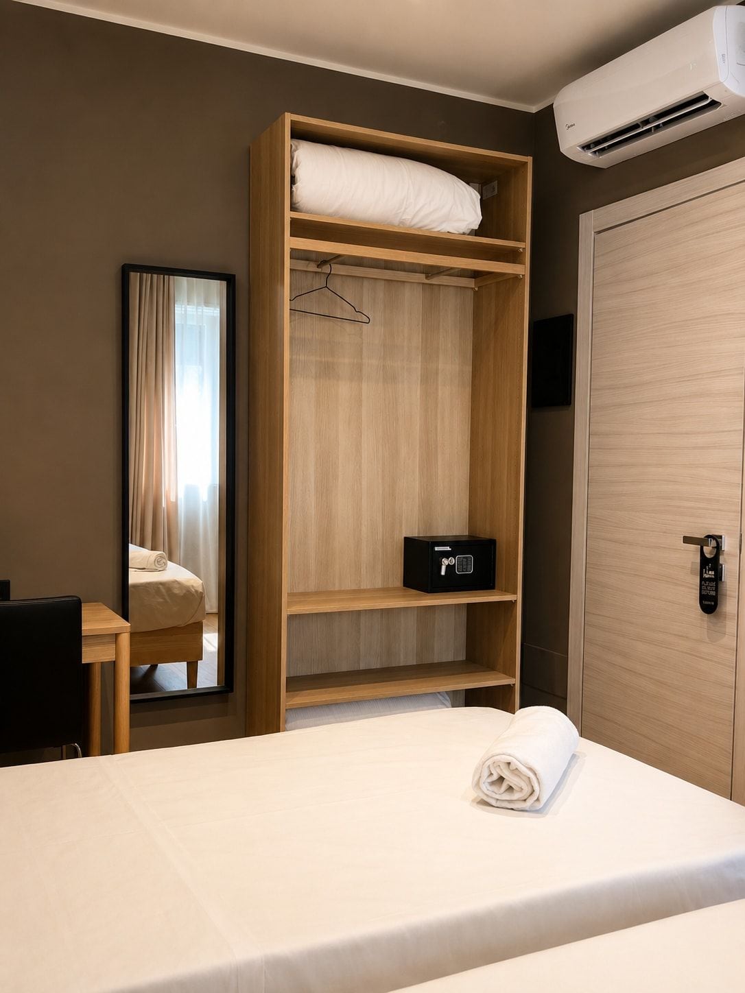 Una camera d'albergo con un letto, un armadio in legno, una cassaforte, uno specchio e un condizionatore d'aria.