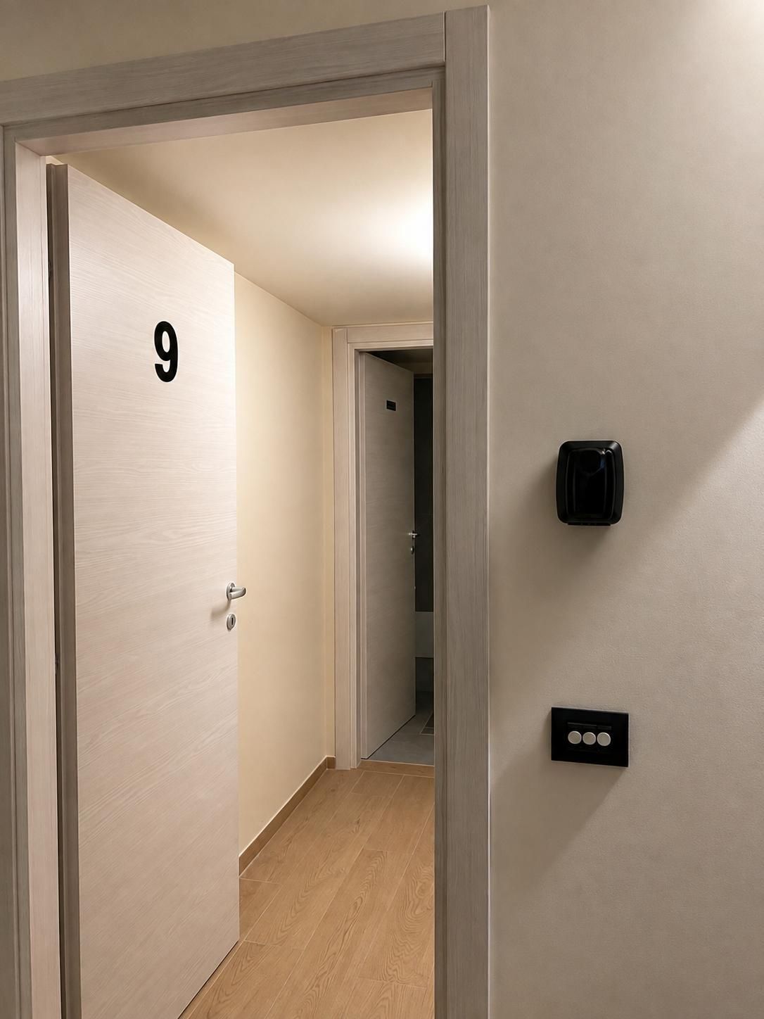 A hallway with a door labeled '9', a wall-mounted intercom, and a light switch.