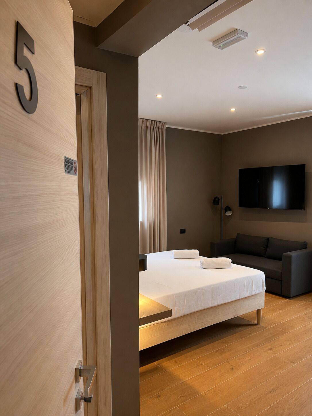 A hotel room with a bed, a sofa, a television, and a door with a number.
