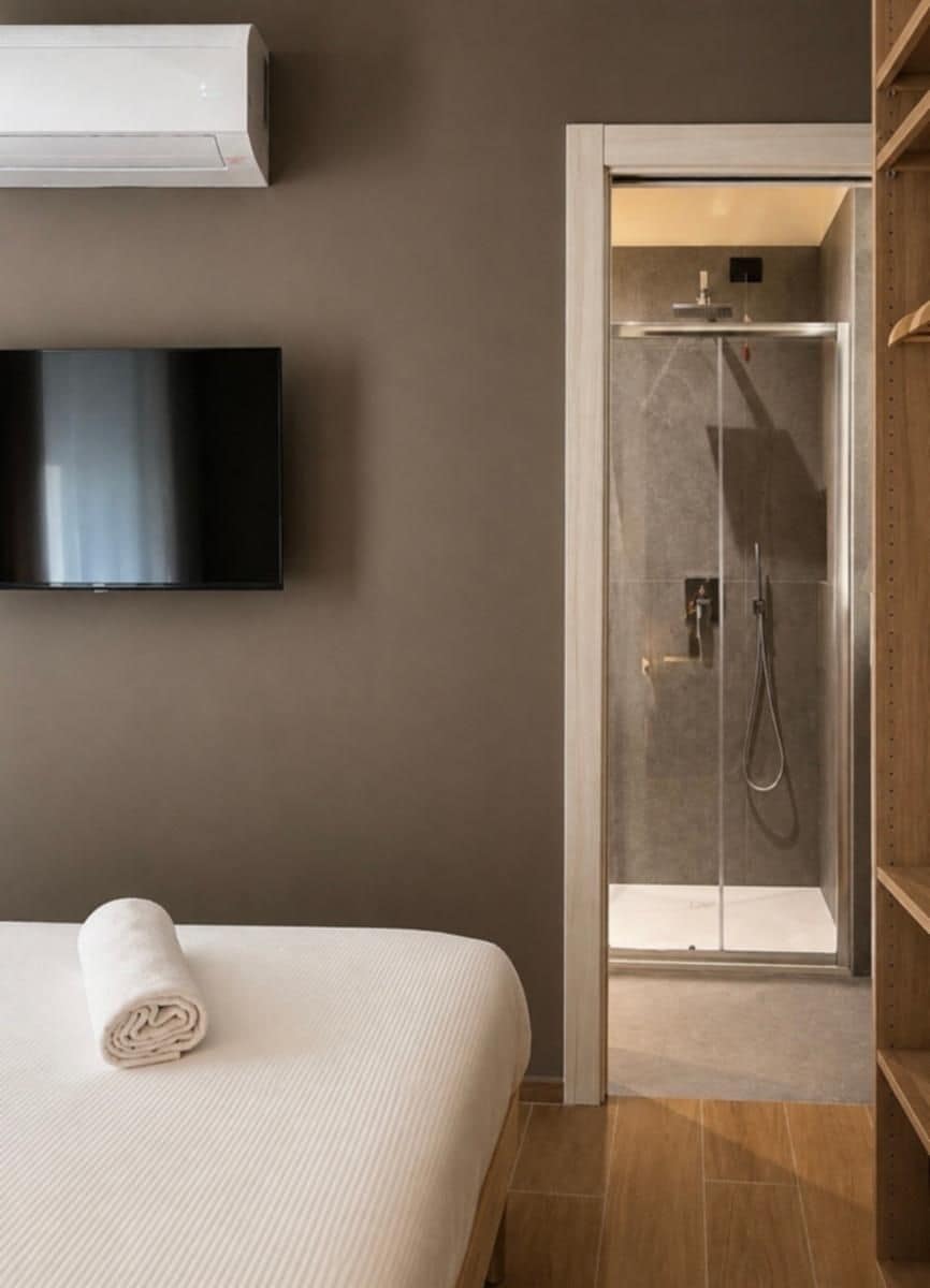 Una camera d'albergo con un letto, una televisione, una doccia e un condizionatore d'aria a parete.