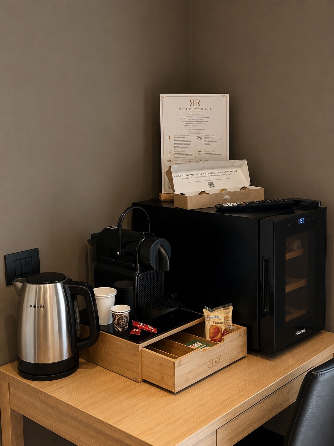 Un bureau dans une chambre d’hôtel, avec une machine à café, un plateau contenant des tasses à café, une boîte de thé et une horloge numérique.