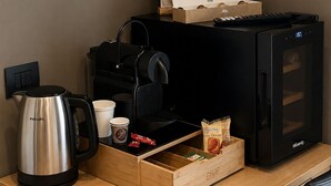 Un bureau dans une chambre d’hôtel, avec une machine à café, un plateau contenant des tasses à café, une boîte de thé et une horloge numérique.