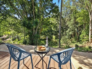 Eine Terrasse mit zwei Stühlen und einem Tisch, mit Blick auf ein bewaldetes Gebiet, im Hintergrund eine Brücke.