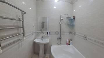 Een badkamer met een bad, een wastafel, een douche en een glazen plank.