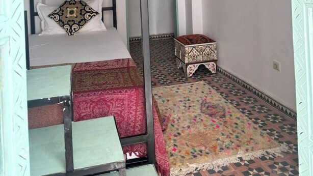Una habitación con una cama litera, un tapete estampado, un taburete pequeño y un techo decorativo.