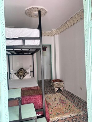 Een kamer met een stapelbed, een kamerkleed met een patroon, een klein krukje en een decoratief plafond.