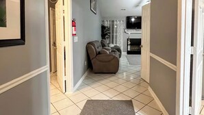 A hallway with a grey carpet leading to a living area with a sofa and a fireplace.
