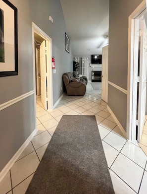 A hallway with a grey carpet leading to a living area with a sofa and a fireplace.