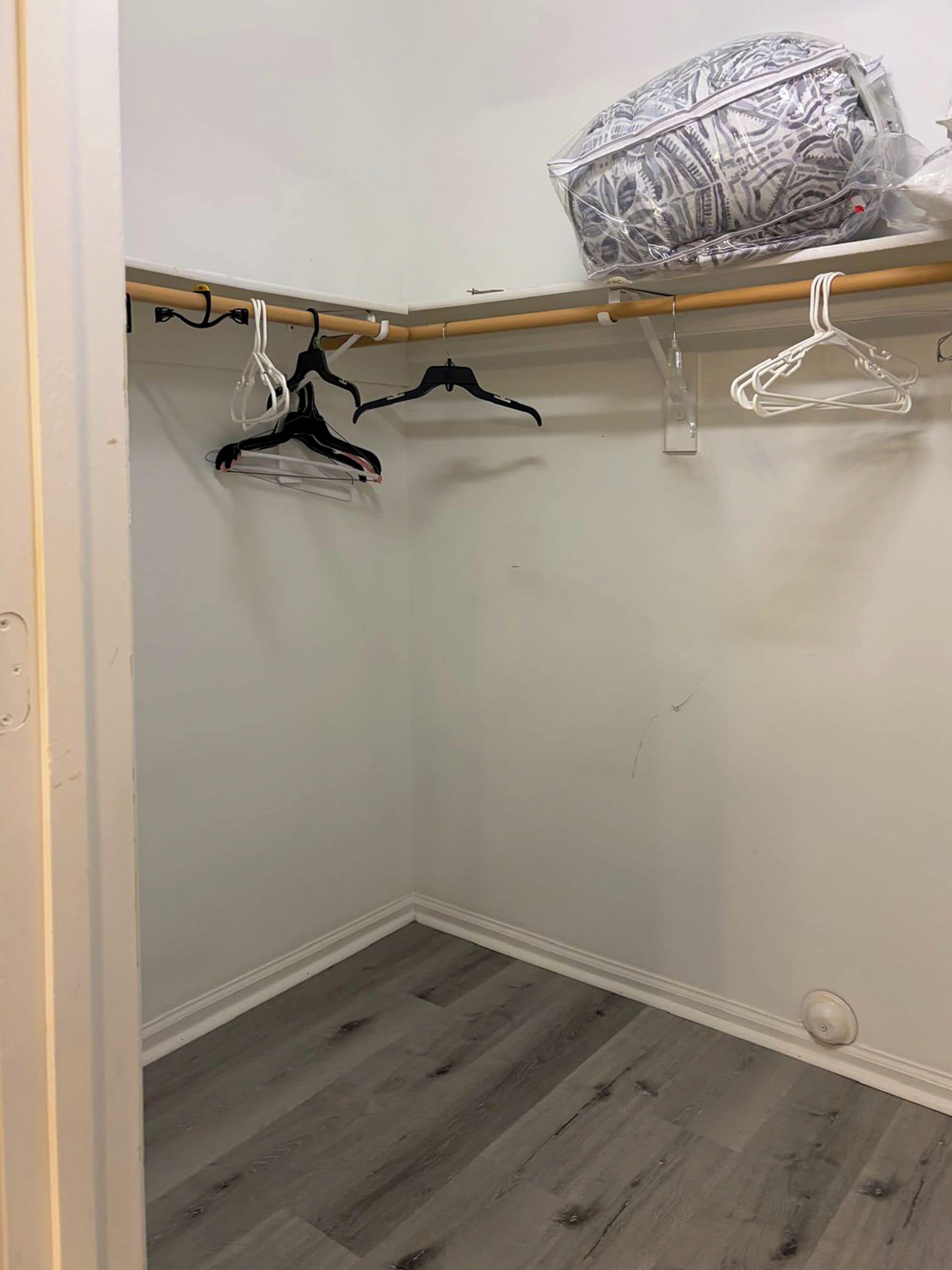 A closet with wooden flooring, white walls, and a wooden rod with hangers.