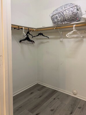 A closet with wooden flooring, white walls, and a wooden rod with hangers.