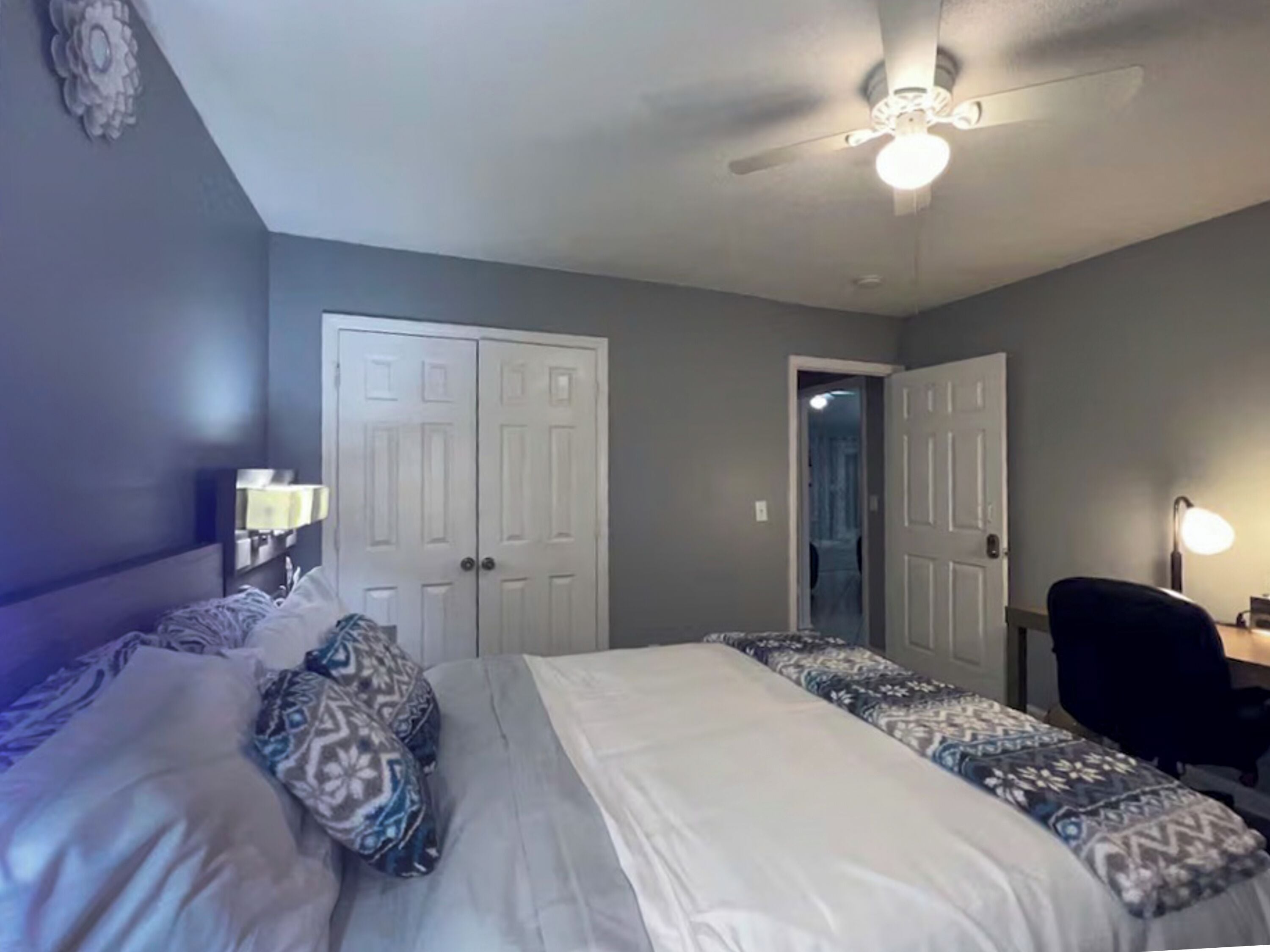 A bedroom with a bed, a desk, and a ceiling fan.