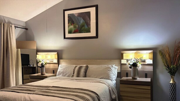 A hotel room with a large bed, bedside tables with lamps, a flat-screen TV, and a framed picture on the wall.