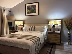 Ein Hotelzimmer mit einem großen Bett, Nachttischen mit Lampen, einem Flachbildfernseher und einem gerahmten Bild an der Wand.