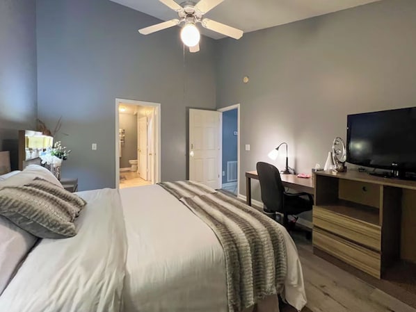 A bedroom with a bed, a desk, a television, and a ceiling fan. - Amos Dr (Greensboro)