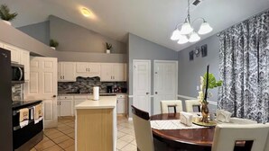 A compact kitchen with a central island, white cabinets, and a dining area with a wooden table and chairs.