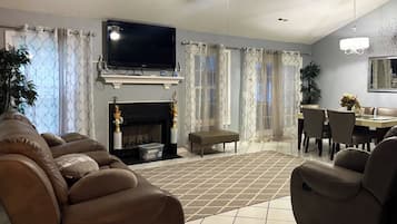 A living room with a fireplace, a television, and a dining area with chairs and a table.