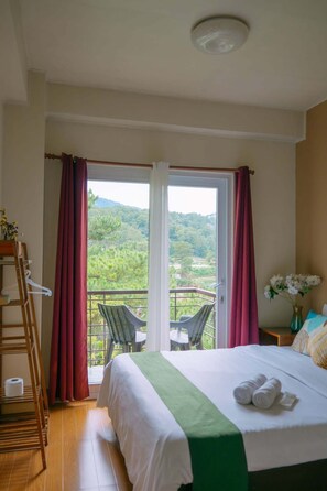 Ein Hotelzimmer mit Bett, einem Balkon mit Stühlen und Blick auf Grünflächen.