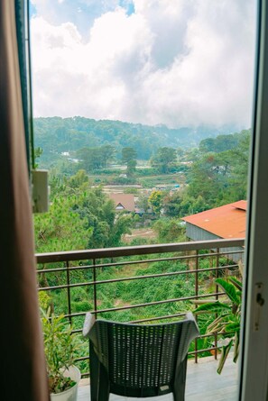 Ein Balkon mit Blick auf eine grüne Landschaft, Bäume und ein Gebäude in der Ferne.