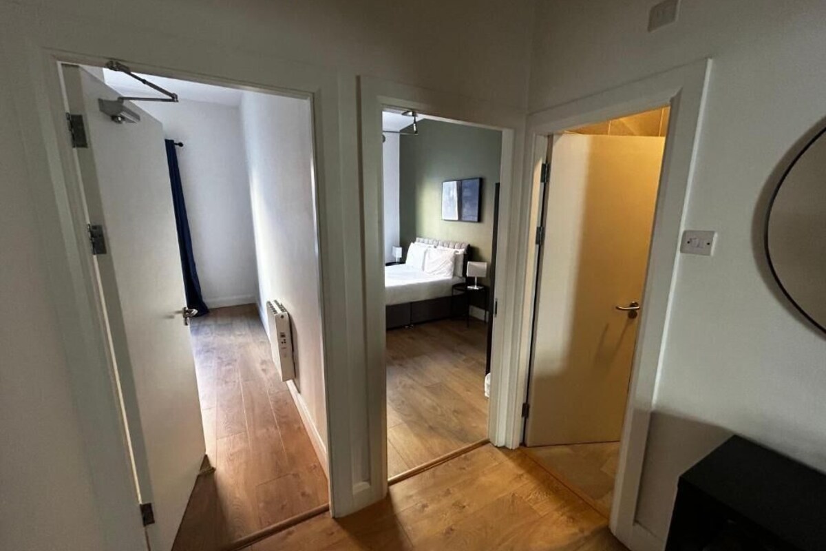 Ein Flur mit Holzboden, der zu einem Schlafzimmer mit Bett und Nachttisch führt.