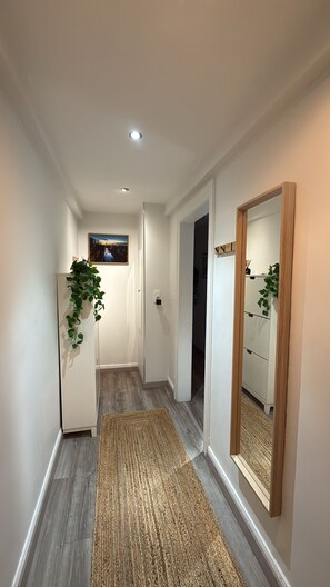 A narrow hallway with a wooden floor, a rug, a refrigerator, a mirror, and a door leading to another room. - Le Cocon des Cordiers, Historic District (Mulhouse)