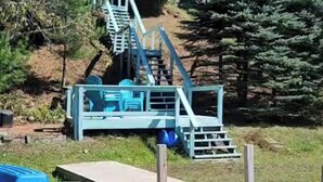 A wooden dock leading to a blue metal structure with stairs, surrounded by trees.
