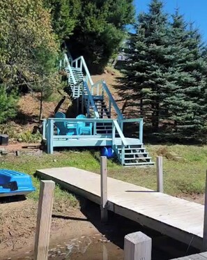 A wooden dock leading to a blue metal structure with stairs, surrounded by trees.