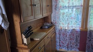 A compact kitchen with wooden cabinets, a countertop with kitchen utensils, and a window with floral curtains.