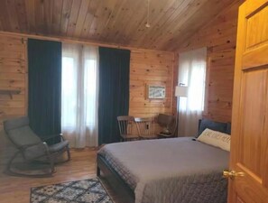 A wooden-paneled room with a bed, two chairs, a small table, and a lamp.