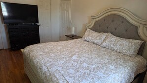 Quarto com cama, televisão, cômoda e mesa de cabeceira.