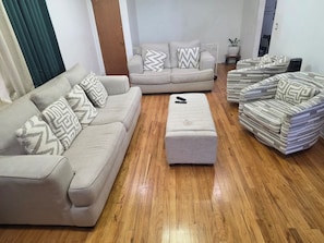 A living room with a beige sofa, a matching ottoman, and a striped armchair. - Serene Oasis - near JFK Airport, LIRR Train & USB (Queens)