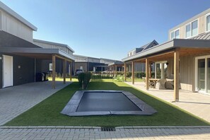 A residential area with a central lawn, a trampoline, and outdoor seating under pergolas. - Villa in Kamperland with swimming pool (Kamperland)