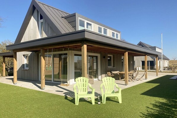 A modern house with a covered patio, two chairs, and a lawn. - Villa in Kamperland with swimming pool (Kamperland)