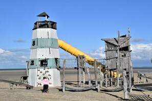 Une plage avec un phare et des structures de jeux en bois.